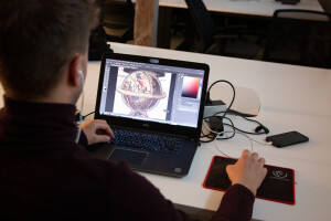 Widoczny od tyłu mężczyzna pracujący na laptopie. Na monitorze fragment ryciny przedstawiającej kulę ziemską.